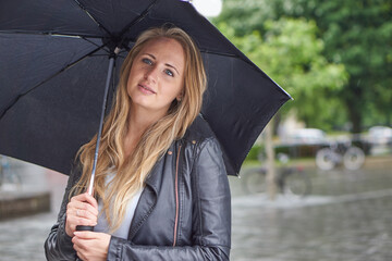 Blonde Frau mit Schirm im Regen