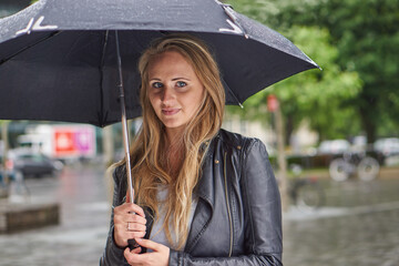 Blonde Frau mit Schirm im Regen