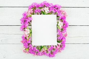 Fototapeta premium Frame made of pink flowers and card on white wooden background. Flat lay, top view.