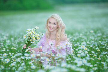 Attractive blonde in chamomile field. Young woman in wreath surrounded by chamomiles wearing stylish pink dress enjoying summer spring