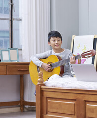 teenage  Asian boy learning, practicing playing guitar at home