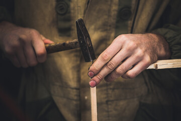 Мan clogs a nail wooden frame for bees. Men's hands with long thin fingers hold wooden frame.