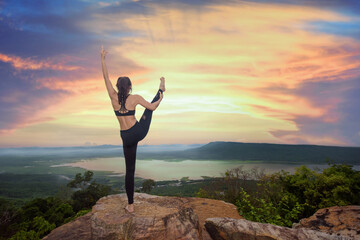young woman practice yoga on high stage of rock with mountain and river in bottom background