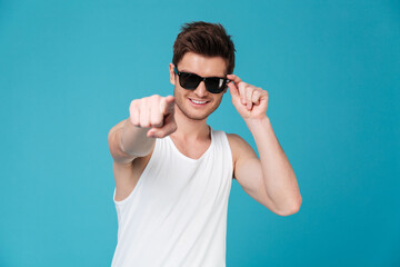 Cheerful guy in sunglasses and singlet pointing finger at camera