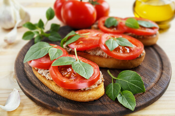 Bruschetta with liver pate, tomatoes and basil on a wooden board. Traditional Italian snack. Close-up.