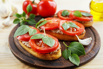 Bruschetta with liver pate, tomatoes and basil on a wooden board. Traditional Italian snack. Close-up.