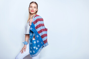 Beautiful blonde girl holding denim vest with american flag on shoulder and looking at camera