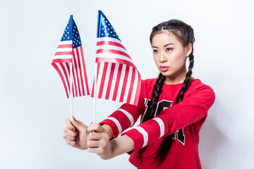 Beautiful asian girl in patriotic outfit holding american flags and looking away