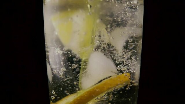 In a glass with soda ice and lemon drop the straw on a black background. Slow motion