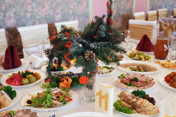 Card with number 11 stands before bouquet of fir branches in the middle of dinner table