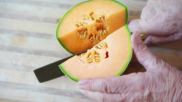 A man cuts up a cantaloupe on a cutting board