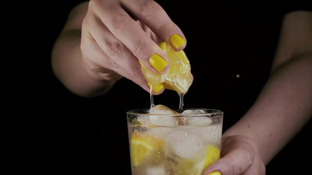 Slow motion. Female hands squeeze out lemon juice from a slice into a glass with lemon water and ice