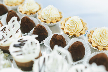 Cookies covered with white icing and cupcakes with white cream served on long glass dish
