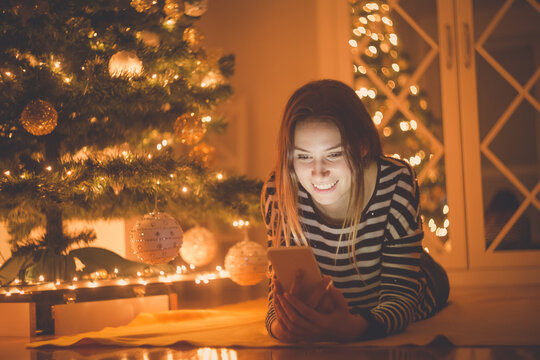 Young female using smartphone next to the Christmas tree at home