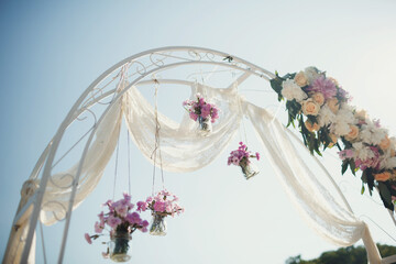 Glass bottles with pink flowers hang from wedding altar