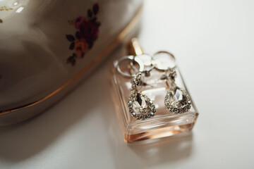 Wedding rings and crystal earrings lie on parfume bottle