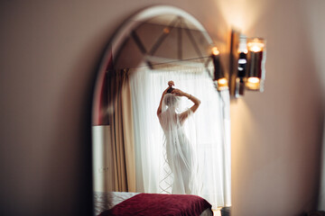 Reflection of bride in a veil standing before a window