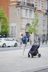 A young woman with a baby photographing herself on the streets of London. United Kingdom.