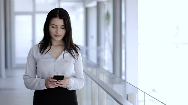 Woman standing and typing on her mobile phone in business building
