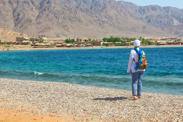 Young Lady Standing by the Cottage in a Camp in Sinai, Taba desert with the Background of the Sea and Mountains.