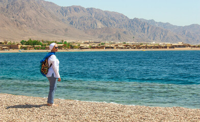 Young Lady Standing by the Cottage in a Camp in Sinai, Taba desert with the Background of the Sea and Mountains.