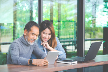 Smiling Attractive mature man with white stylish short beard using tablet with charming woman teenage. Serving internet via his gadget. Teaching old man using social network technology