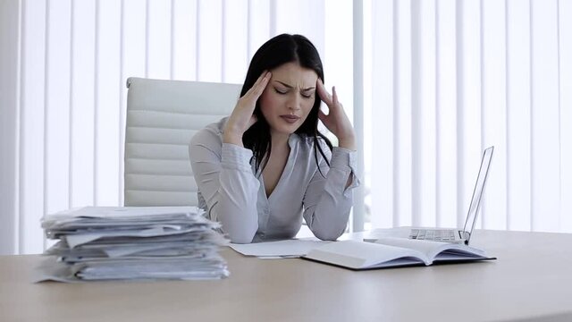 Woman in office working with papers and having headache