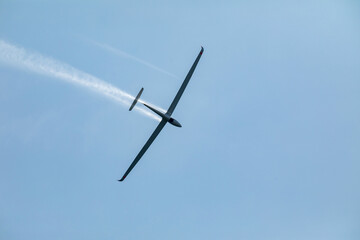 A glider flying in the blue sky ejects the water before the landing.