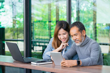 Smiling Attractive mature man with white stylish short beard using tablet with charming woman teenage. Serving internet via his gadget. Teaching old man using social network technology