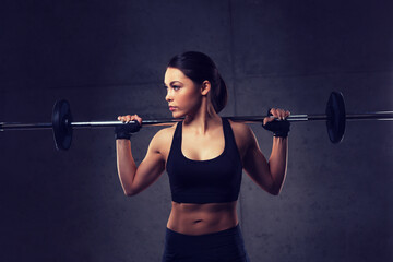 young woman flexing muscles with barbell in gym