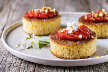Pieces of homemade semolina cake with strawberry and pistachio decorated flowers of cherry on a rustic vintage wooden table. Selective focus 