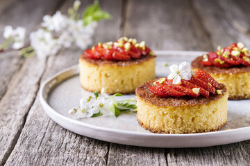 Pieces of homemade semolina cake with strawberry and pistachio decorated flowers of cherry on a rustic vintage wooden table. Selective focus 