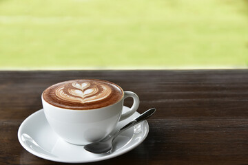A cup of coffee with heart pattern in a white cup on wooden background