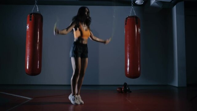 Young woman boxer jumping on a skipping rope in a dark hall