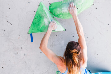 Athlete Woman exercising at a sport climbing wall in a bouldering gym, back view