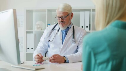Caucasian male doctor sitting in his offise, telling about drugs and giving drugs to female young patient. Indoor.
