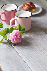 Two pink cups with milk on a white wooden table