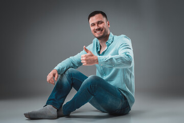 Appealing casual young man sitting on the floor, looking to the camera smiling