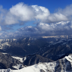Fototapeta premium Sunlit winter mountains in clouds, view from off-piste slope