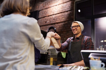 woman taking paper bag from seller at cafe