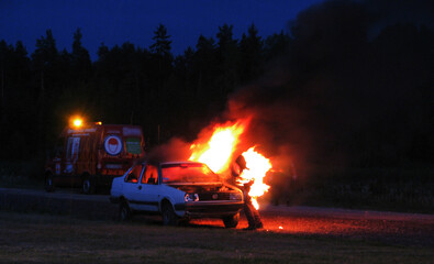 Burning car on the road in the night, burning man