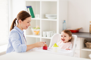 Obraz na płótnie Canvas happy mother feeding baby with puree at home