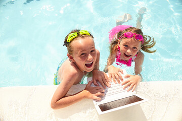 Happy little boy and girl using laptop in pool
