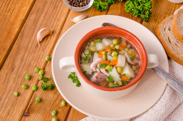 Chicken soup with green peas and vegetables in a bowl on a wooden background