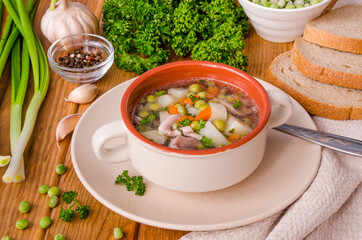 Chicken soup with green peas and vegetables in a bowl on a wooden background