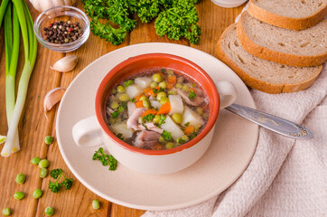 Chicken soup with green peas and vegetables in a bowl on a wooden background