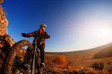 Naklejka na ściany i meble low angle view of cyclist riding mountain bike on rocky trail at sunrise