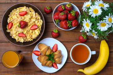 Healthy breakfast: corn flakes, strawberries, juice, tea and croissant.