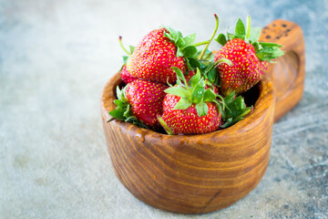 Close up fresh delicious strawberry in wooden bowl on gray table background. Summer food berries. Healthy food content