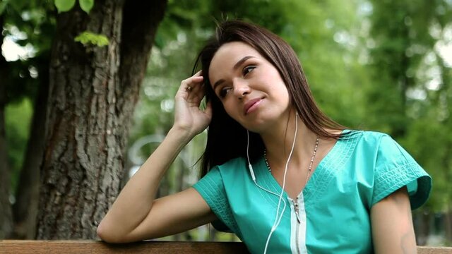 Pretty dark-haired young woman listening to the music on headphones in a park on a sunny day. HD